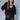 A woman with long brown hair and bangs models the Sanctuary Clothing meow cardi kitty camo leopard print cardigan with black faux leather pants and a black belt against a plain light gray background.