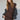 A woman with long brown hair wears the Sanctuary Clothing autumns best sweater dress in cocoa plaid, featuring a thigh-high slit, styled with a black denim jacket over her shoulders, posing against a neutral background.