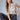 A woman with long, light brown hair and bangs sits on an orange chair, confidently wearing the Sanctuary Clothing fuzzy leopard shell mother leo top and black high-waisted jeans with a black belt against a plain background.