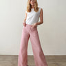 A woman with long blonde hair wears the Sanctuary Clothing marine full length semi high rise pant in galley stripe and a sleeveless white top, standing on a polished concrete floor against a plain light-colored wall.