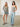 Two women stand indoors on a concrete floor, both wearing light blue denim bottoms and striped, cream-and-black tops. One wears shorts and sandals, the other wears wide-leg pants and sandals.