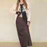 A woman with long brown hair and bangs poses indoors, wearing the Sanctuary Clothing 'everyday maxi skirt semi sweet,' a black and white sweater, off-white jacket, and black ankle boots. One hand is in her pocket.