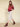 A woman stands against a beige background wearing the Sanctuary Clothing satin track jacket in crimson, paired with a shimmery white midi skirt, burgundy socks, and matching heeled shoes. Her hands are tucked in her jacket pockets.