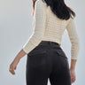 A woman with long dark hair, wearing a cream textured knit sweater and Sanctuary Clothing’s corduroy Hayden bootcut pant in Semi Sweet, stands with her back to the camera against a light neutral background.